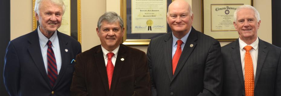 Four men--Chair Powers, Commissioner Whitfield, Secretary of State Mark Hammond, and Commissioner Caston. All are wearing suits and ties. 